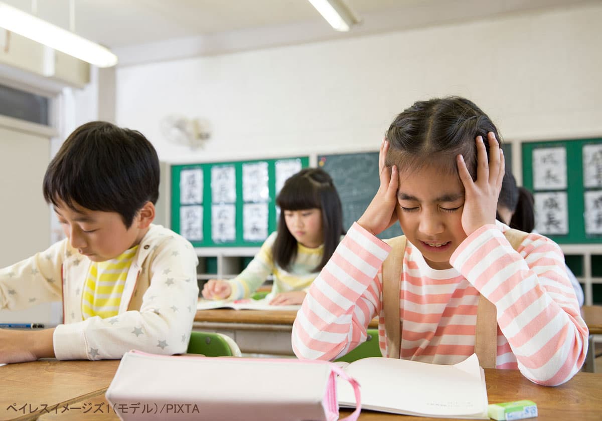 教室で頭を抱えて辛そうな小学生の女の子
